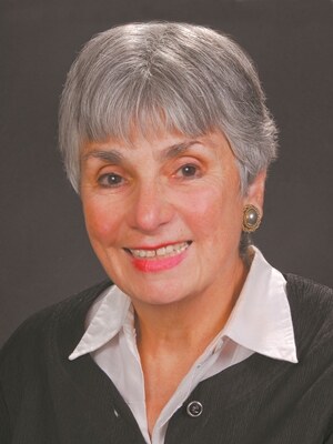 A studio portrait of Toby Carliner Sanchez, smiling, with short silver hair.